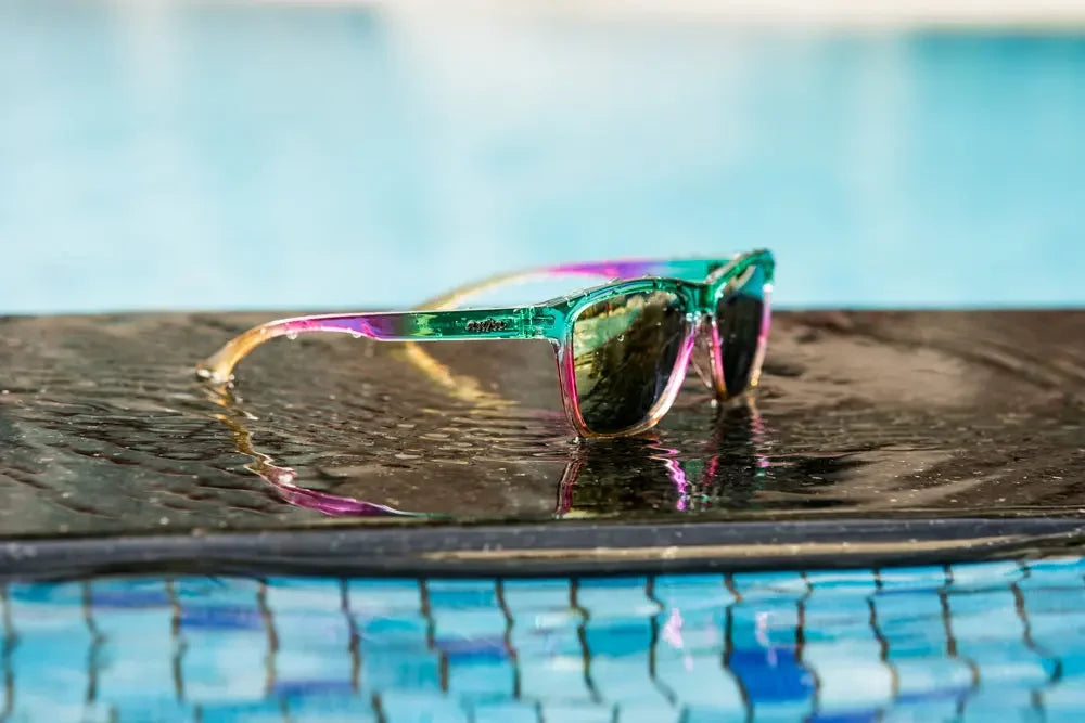 Colorful polarized sunglasses with transparent turquoise and pink frame on wet poolside surface.