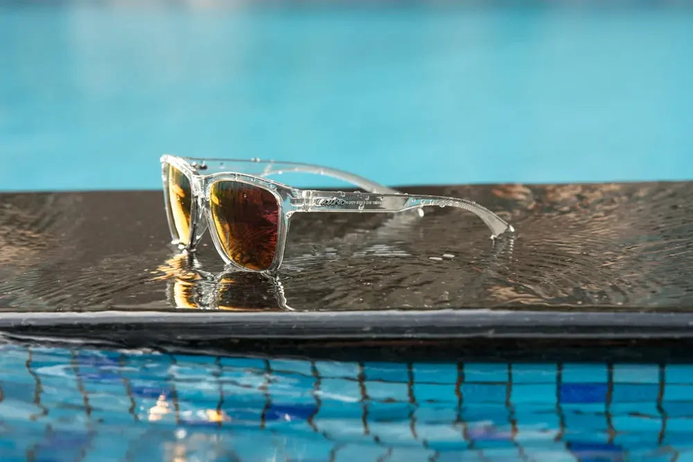 Polarised sunglasses with clear frames on wet poolside, reflecting in water, summer accessory