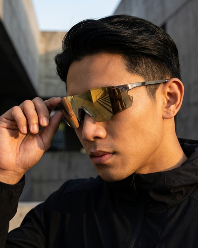Man adjusting gold reflective sunglasses against a blurred outdoor background