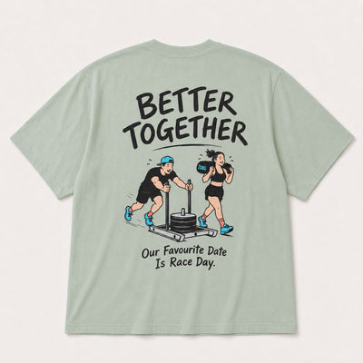 A sage green short-sleeve t-shirt shown from the back, featuring a large graphic print of a man and a woman exercising together with the text 'BETTER TOGETHER' and 'Our Favourite Date Is Race Day.'.