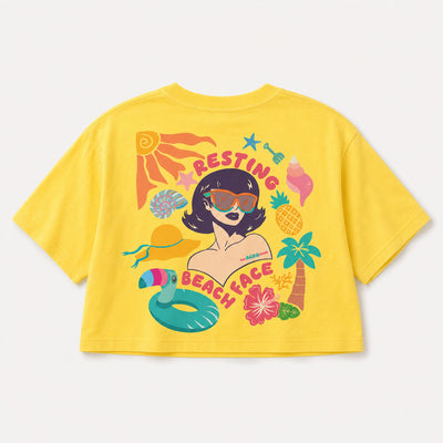 A bright yellow short-sleeve crop top t-shirt featuring a colorful retro-style graphic of a woman with sunglasses surrounded by beach-themed illustrations like a palm tree, pineapple, and pool float, with the text 'RESTING BEACH FACE'.