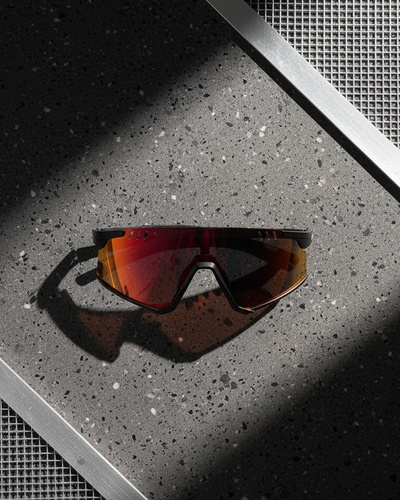 Sunglasses with red lenses on a textured surface with carbon fiber frames